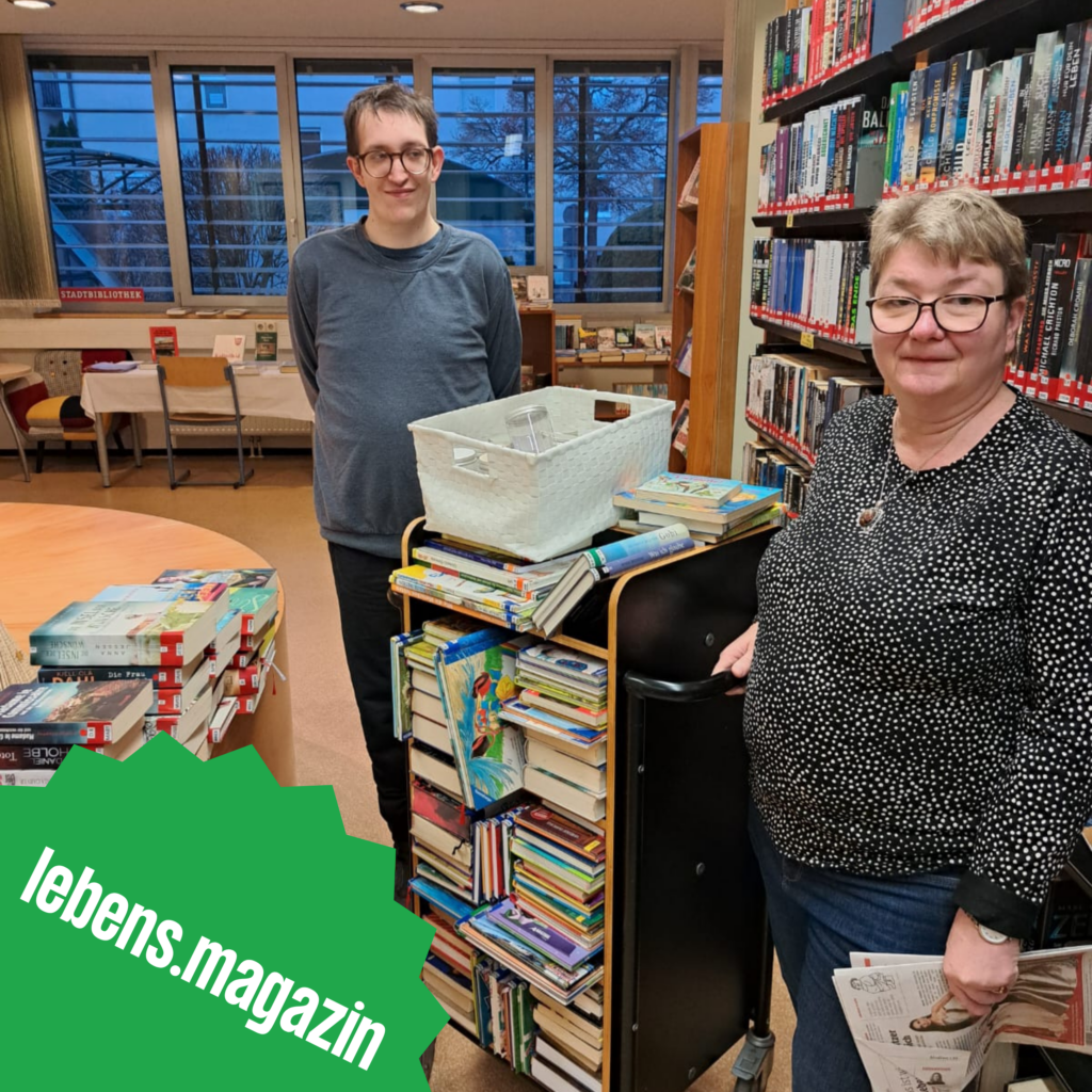 Lukas Hubmann und Sylvia Wielender bei der Arbeit in der Stadtbibliothek Knittelfeld. Sie stehen vor Bücherregalen und schauen in die Kamera.